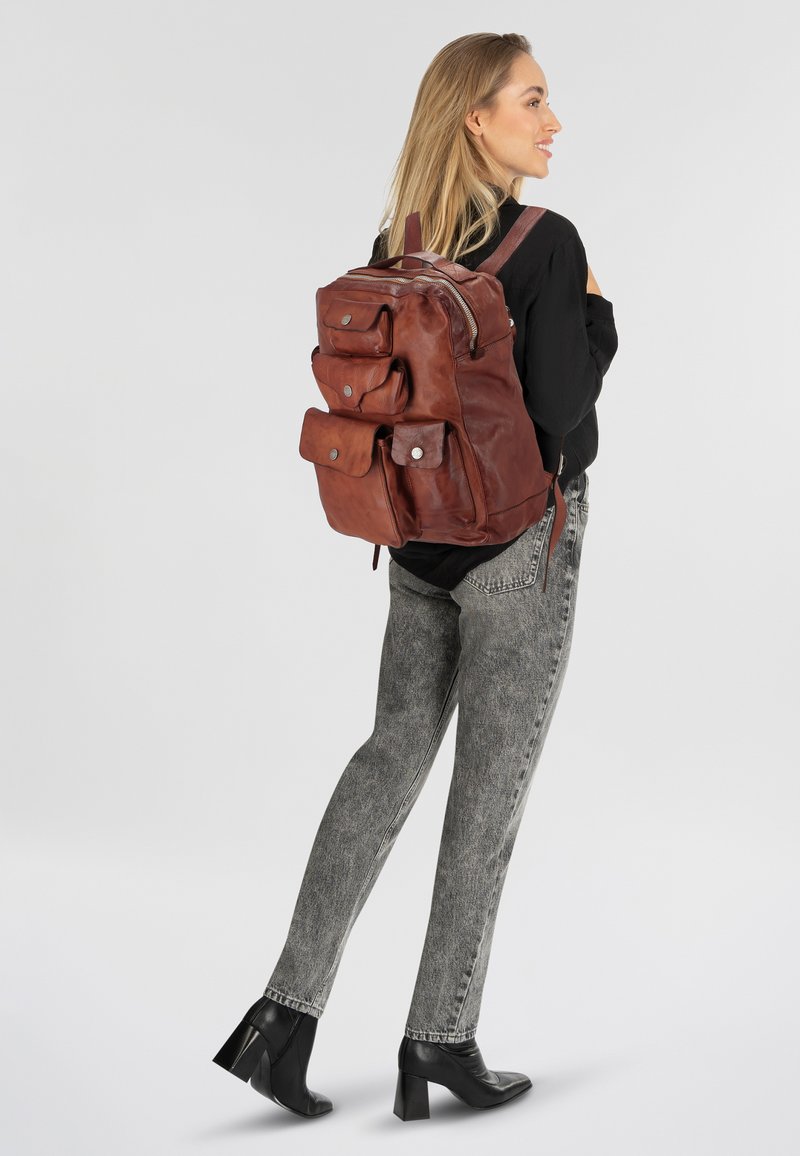 Sac à dos en cuir marron avec plusieurs poches avant, des sangles réglables et une fermeture éclair. Texture lisse et design durable.