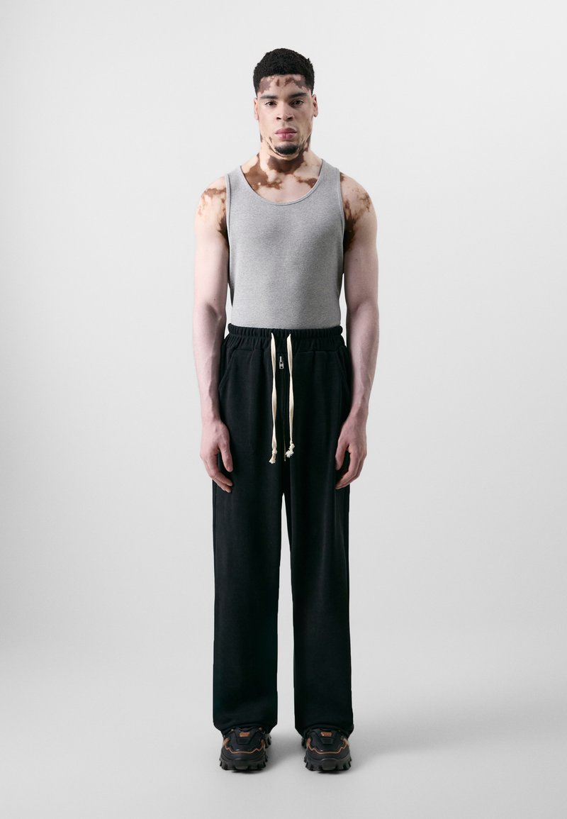 Gray tank top, black sweatpants with elastic waistband and white drawstring, and chunky black shoes. Smooth texture, relaxed fit.
