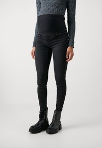 Zwarte zwangerschaps skinny jeans met een rekbare tailleband, gecombineerd met zwarte enkellaarsjes met een stevige zool en ritsdetail.