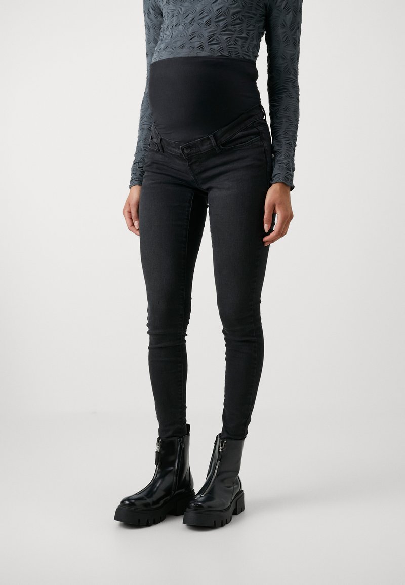 Zwarte zwangerschaps skinny jeans met een rekbare tailleband, gecombineerd met zwarte enkellaarsjes met een stevige zool en ritsdetail.