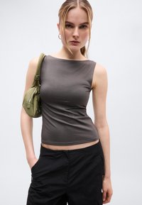 Haut sans manches gris foncé en tissu lisse, avec un col rond. Associé à un pantalon ample noir et à un sac à main vert avec des accents.