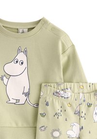 Vihreä huppari, jossa on kuvio kartonkihahmosta, ja siihen sopivat housut, joissa on leikkimielinen kuvio puista ja eläimistä. Pehmeä puuvillakangas.