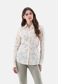 Camicia a maniche lunghe con bottoni in tessuto bianco trasparente con motivo floreale giallo e grigio. Presenta un colletto classico e maniche con polsini.