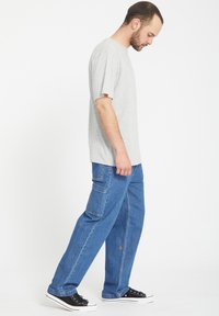 Camiseta gris de algodón combinada con pantalones cargo de denim azul de corte holgado que cuentan con bolsillos laterales. Zapatillas negras con cordones completan el atuendo.