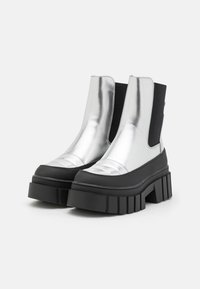Botas metálicas plateadas hasta el tobillo con una suela de plataforma negra y gruesa y paneles laterales elásticos. Textura suave con punta redonda y detalles cosidos.