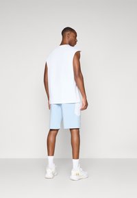 White sleeveless shirt and light blue shorts with a side pocket detail. The outfit is paired with white and yellow athletic shoes.