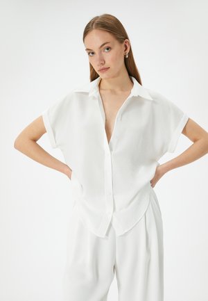 Camicetta bianca a maniche corte con bottoni, realizzata in materiale leggero, caratterizzata da un colletto, una vestibilità ampia e un design a V profonda.