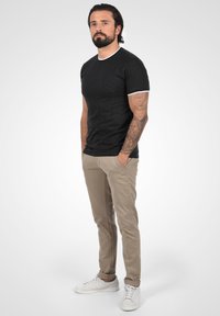 Camiseta negra texturizada con cuello blanco, combinada con pantalones chinos beige claros. Zapatillas blancas completan el atuendo.