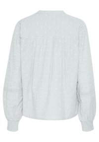 Lichtgrijze blouse met lange mouwen, voorzien van ge-mêleerde bloemenpatronen, een geplooide achterkant en gesmokte manchetten. Heeft een ronde kraag en fijne kantafwerking.