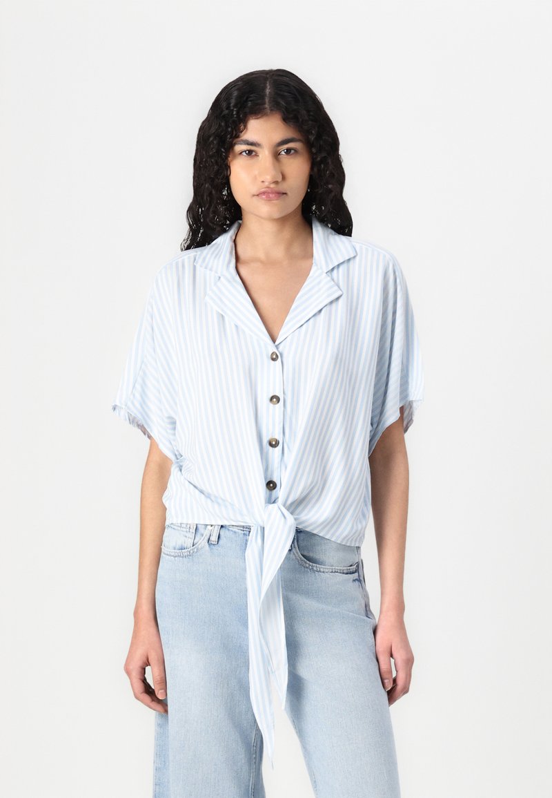 Button-up, short-sleeve shirt in light blue with white stripes. Features a knotted front design and a collar. Smooth fabric with a relaxed fit.