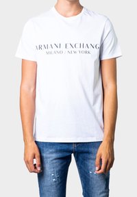 Bílá bavlněná tričko s potiskem "ARMANI EXCHANGE MILANO / NEW YORK" v černé barvě, kulatý výstřih, krátké rukávy, přiléhavý střih.