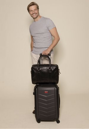 Black leather briefcase with dual handles atop a black, hard-shell suitcase featuring textured chevron design and smooth wheels.