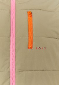 Giacca puffer color khaki con zip rosa e arancioni; presenta una tasca sul petto con zip e il logo "ROXY" in rosso. Texture liscia, design trapuntato.