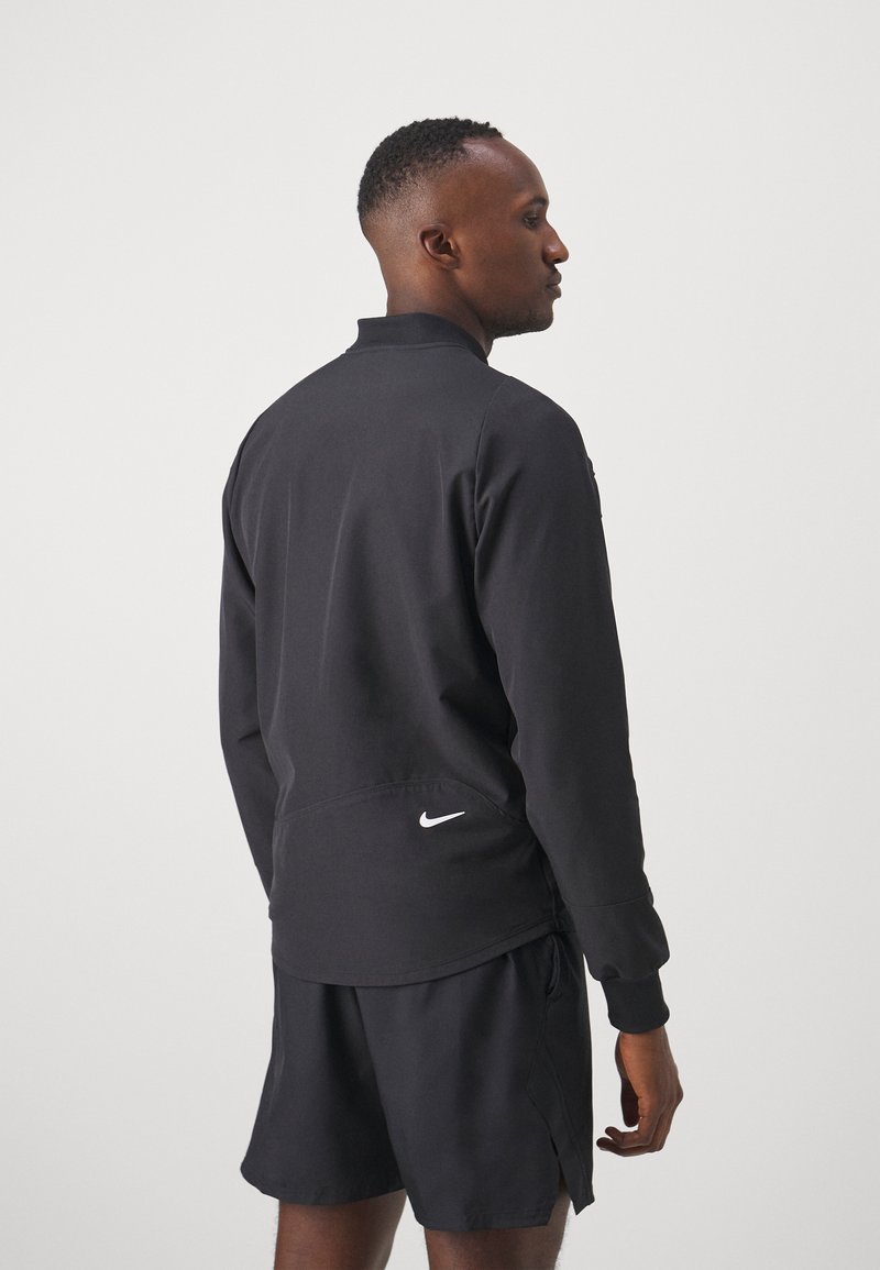 Zwarte sportjack met een hoge kraag en lange mouwen, voorzien van een wit Nike-logo op de rug en zijzakken.