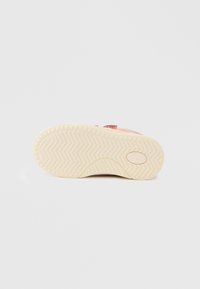 Εξωτερική σόλα αθλητικού παπουτσιού από κρεμ καουτσούκ με ζιγκ ζαγκ σχέδιο πέλματος. Διαθέτει κυκλικό λογότυπο και λεία υφή. Χωρίς ορατά σημάδια.