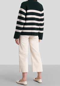 Raidallinen villapaita tummanvihreänä ja vaaleanbeigenä, valmistettu teksturoidusta neuleesta, jossa on pudotetut olkapäät. Yhdistetty valkoisiin lyhyisiin housuihin ja beigeihin ballerinatossuihin.