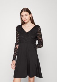 Vestido preto com um top de renda, featuring um decote em V, mangas longas e uma saia rodada a partir da cintura. Tecido suave com uma sobreposição de renda texturizada.