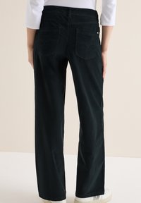 Jean noir à jambe large avec un design épuré, deux poches arrière avec des coutures arrondies et une texture subtile. Ceinture et longueur standard.