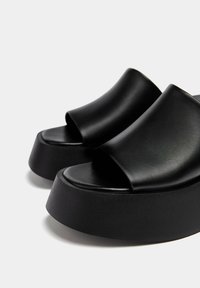 Sandali platform neri con tomaia in pelle liscia, design open toe e suola spessa e lavorata. Caratterizzati da una punta arrotondata e uno stile minimalista.