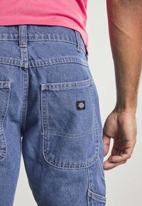 Blå denim cargo byxor har flera fickor, en liten svart etikett på bakfickan och kontrasterande sömnadsdetaljer.