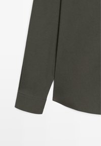 Dunkelgrünes Langarmshirt mit weicher Textur, das über eine strukturierte Manschette und einen abgerundeten Saum verfügt. Glattes Gewebe mit minimaler Detailgestaltung.