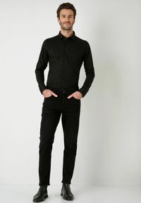 Zwarte overhemd met knopen en een klein wit stippenpatroon, gecombineerd met zwarte denim jeans en zwarte enkellaarsjes; slim fit, gladde textuur.