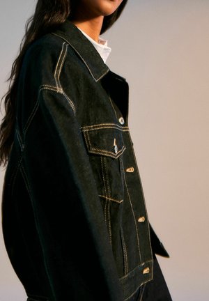 Veste en denim noir avec des coutures jaunes contrastées, deux poches avant et des boutons métalliques. Dotée d'un col classique et d'une coupe décontractée.