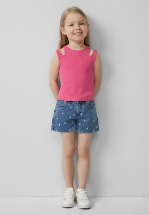 Roze mouwloze top met uitgesneden schouders, gecombineerd met denim shorts met bloemen- en fruitprints, aangevuld met witte sneakers.