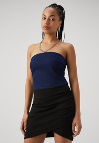 Navy denim strapless top paired with a black ruched mini skirt. The outfit features a silver chain necklace for added detail.