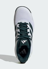 Chaussure de sport blanche avec des accents verts, tige en mesh, quatre rayures noires, semelle en caoutchouc et languette texturée. Présente un logo au niveau du talon.