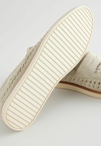 Sneaker in suede beige con un design intrecciato sul lato e una suola in gomma bianca testurizzata con scanalature per una migliore aderenza.