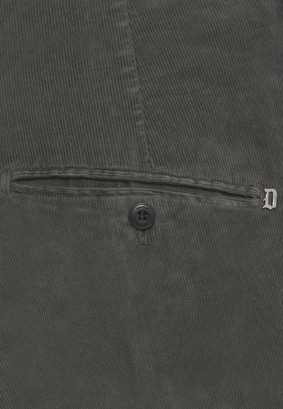 Tessuto di velluto a coste grigio scuro con una tasca a filetto orizzontale, un singolo bottone nero e un piccolo emblema metallico a forma di "D" sul bordo destro della tasca.