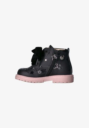 Stivaletto alla caviglia in pelle verniciata nera con fori a forma di stella, suola rosa, zip laterale e grande fiocco nero frontale. Design chunky, superficie texturizzata.