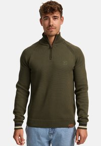 Donkergroen ritsvest met geribbeld textuur, voorzien van een hoge kraag, contrasterende gestreepte manchetten en een logopatch op de zoom.