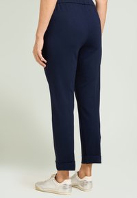 Pantalones azul marino de corte estrecho con cintura elástica, puños doblados y textura suave. Combinados con zapatillas deportivas con acentos plateados.