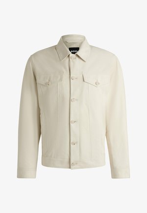 Vaalea beige farkkutakki, jossa on klassinen kaulus, nappikiinnitys edessä, kaksi rintataskua ja hienovaraiset tikkausten yksityiskohdat. Silkkinen rakenne.