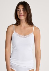 Camisole blanche en tissu doux, avec un délicat revers en dentelle le long de l'encolure et des bretelles spaghetti réglables.