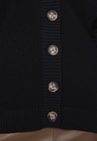 Granatowy dzianinowy kardigan z sześcioma dużymi okrągłymi guzikami oraz ściągaczem u dołu i na mankietach. Tekstura jest lekko wypukła z tkanym wzorem.