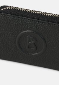 Cartera de cuero negra con una superficie texturizada, que presenta un emblema redondeado en relieve con la letra "B" y una cremallera plateada.