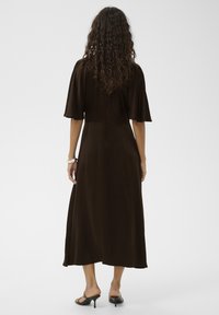 Robe marron mi-longue avec manches courtes et larges, coupe décontractée et texture lisse, avec un détail discret de couture au dos.