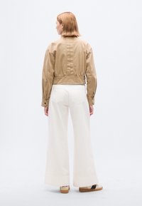 Μπεζ μπουφάν τύπου bomber με κοντό σχεδιασμό, υφασμάτινη υφή και ελαστικό τελείωμα. Συνδυάζεται με λευκά παντελόνια φαρδιάς γραμμής και άνετα παπούτσια.