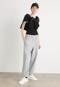 Zwarte fitted top gecombineerd met losse grijze sweatpants, voorzien van een elastische tailleband. Draagt witte sneakers en een zwarte pet. Eenvoudig ontwerp.