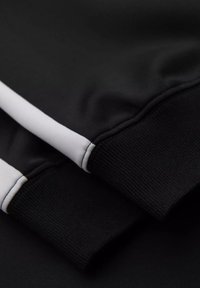 Zwarte sweatshirt manchetten met witte accentstrepen, met een geribbelde textuur bij de randen en gladde stof op het lichaam.