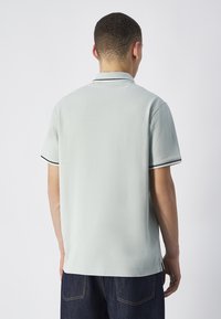 Jasnozielona koszulka polo z teksturowanej tkaniny, krótki rękaw i czarne wykończenia przy kołnierzyku i mankietach. Posiada prosty dół.