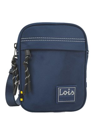 Bolsa de tela suave de color azul marino con costuras en blanco, cierre de cremallera, correa ajustable y un parche de marca. Presenta dos tiradores de cordón negro.
