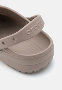 Heledadbeez Crocs paksusega, pehme tekstuuri ja kontuuritud tallaga. Omab laia rihma, millel on logo reljeefselt. 
