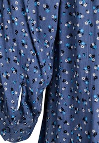 Blauer Stoff mit kleinem schwarzem, weißem und blauem Blumenmuster, zeigt eine lange Manschette mit einem blauen Knopf.