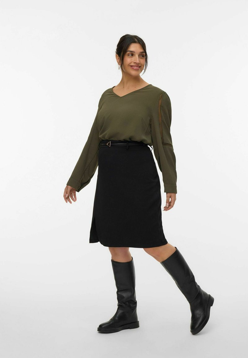 Blouse olive verte à manches longues avec décolleté en V, associée à une jupe noire jusqu'au genou et des bottes en cuir noires hautes. Comprend une ceinture avec une boucle triangulaire.