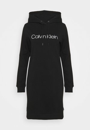 Schwarzes langärmliges Kapuzenkleid mit weißem Calvin Klein-Logo, das mittig auf der Brust platziert ist, und Kordeln, die von der Kapuze herunterhängen.