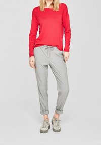 Pull en maille rouge, pantalon ample gris avec cordon de serrage, et baskets gris clair avec une semelle texturée. Tenue décontractée présentée.